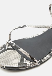 Μαύρο σανδάλι με λεπτά λουριά σε σχέδιο φίδι και τακούνι με το ίδιο σχέδιο.