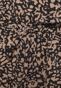 Tissu beige avec imprimé léopard abstrait noir, comprenant une couture piquée et un détail de ceinture nouée.