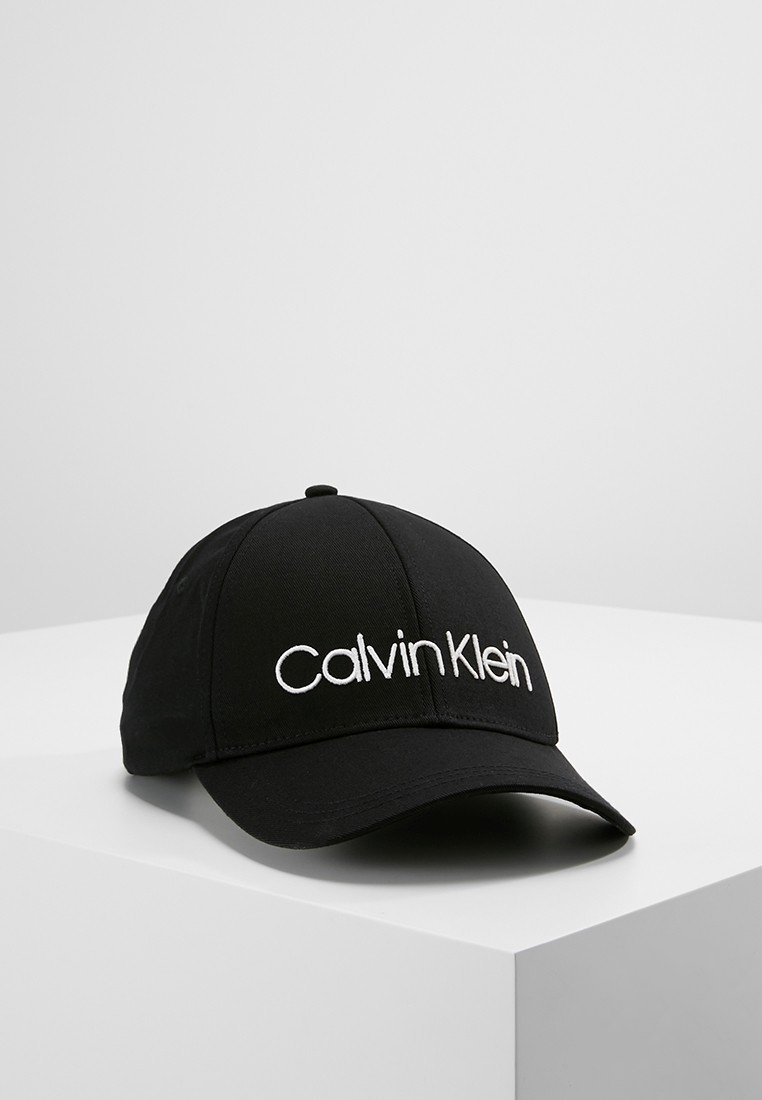 Casquette de baseball noire avec logo Calvin Klein blanc brodé à l'avant, présentée sur une surface blanche devant un fond gris.