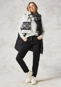 Svart pufferväst över grå tröja; svarta byxor; mönstrad ylleschal i grått och marinblått; vita sneakers. Texturerad, lagerpålagd outfit.