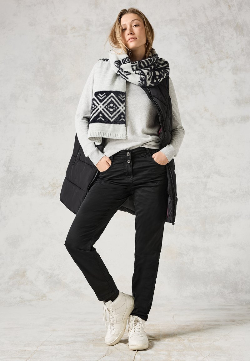 Svart pufferväst över grå tröja; svarta byxor; mönstrad ylleschal i grått och marinblått; vita sneakers. Texturerad, lagerpålagd outfit.