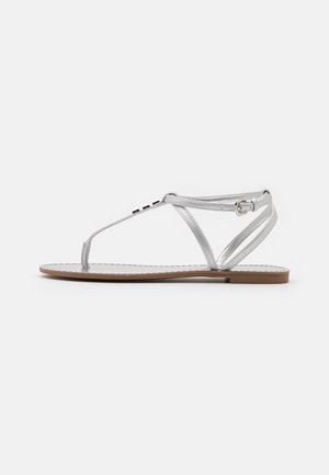 Silver flat sandals with a thong design, featuring thin straps, a small buckle, and metallic accents on the upper. Flat sole, minimalistic style.