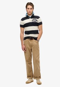 Gestreepte navy en witte polo met kraag, beige chinos en crèmekleurige sneakers. Inclusief horloge en riem, met opgerolde broekspijpen.