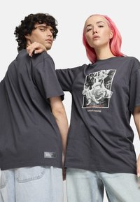 Las camisetas de algodón grises presentan un estampado gráfico en la parte frontal, con el texto "Correr natural", y una etiqueta en el dobladillo. El diseño es de corte holgado.