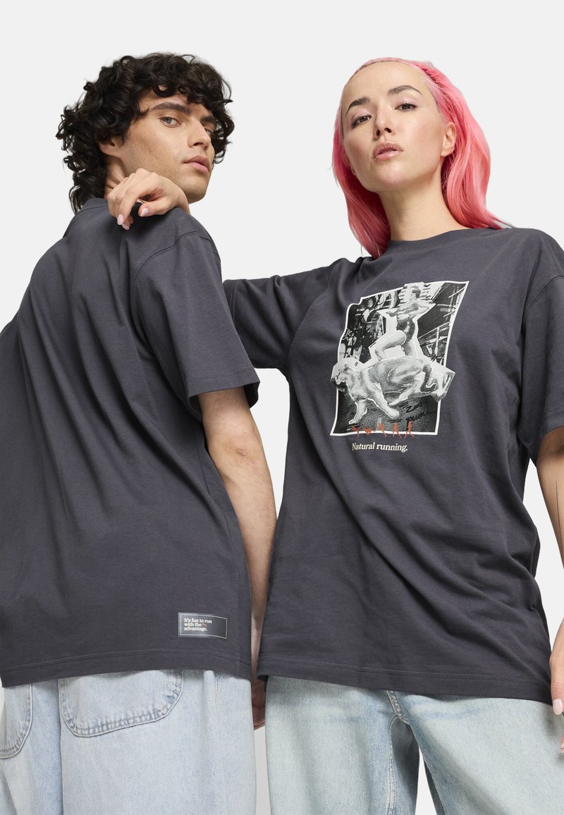 Las camisetas de algodón grises presentan un estampado gráfico en la parte frontal, con el texto "Correr natural", y una etiqueta en el dobladillo. El diseño es de corte holgado.
