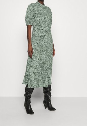 Vestido midi verde con estampado floral, mangas cortas abullonadas, cuello redondo, silueta A-line fluida y combinado con botas negras de caña alta ajustadas.