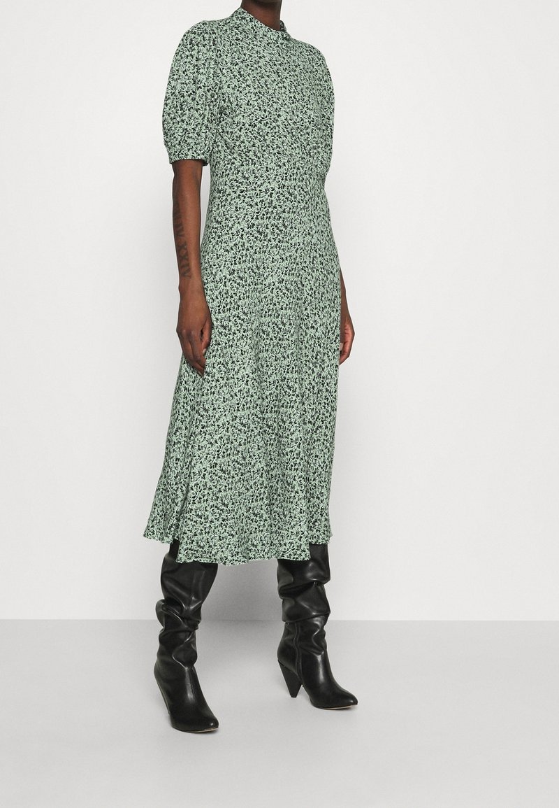 Grön blommig midiklänning med korta puffärmar, rund halsringning, flödande A-linjeform och matchad med åtsittande svarta knähöga stövlar.