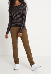 Czarna i biała bluzka w paski z długim rękawem, zestawiona z beżowymi, dopasowanymi spodniami. Dopełnieniem stroju są białe trampki. Tkanina wydaje się gładka i casualowa.