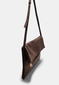 Borsa a spalla in suede marrone con design piatto, patta pieghevole e zip dorata. Cinghia in pelle regolabile per un facile trasporto.