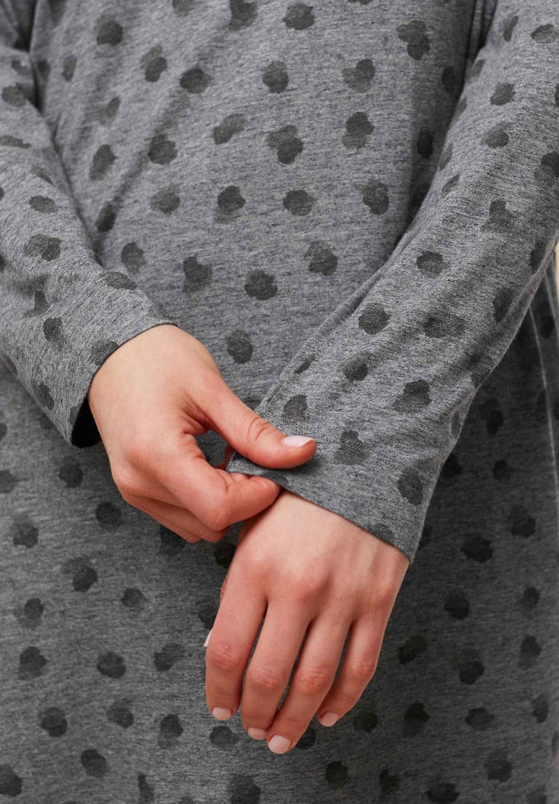 Szary longsleeve z wzorem w kropki w ciemniejszym odcieniu szarości. Tkanina wygląda na miękką i wygodną, z widocznymi detalami mankietów.