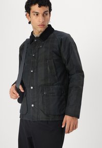 Black plaid jacket made of textured fabric with a corduroy collar, snap buttons, and a front pocket. The model carries a strap bag.