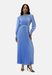 Abito lungo a maniche lunghe con pieghe, di colore azzurro chiaro, con corpetto aderente e vita con cintura. Tessuto liscio; presenta una scollatura curva e polsini arricciati.