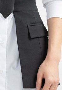 Gilet nero su misura con un design strutturato, dotato di una tasca e una camicia bianca a contrasto sotto. Tessuto liscio e linee pulite.