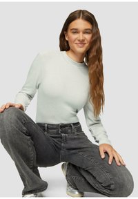 Hellgrünes, geripptes Langarmoberteil, kombiniert mit dunkelgrauen, hochgeschnittenen Jeans. Das Outfit hat einen lässigen Schnitt und eine glatte Textur.