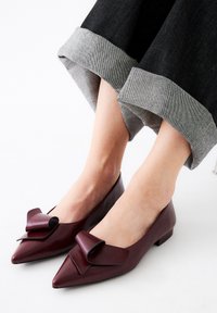 Bailarinas de cuero burdeos con punta afilada y un gran lazo en el empeine, combinadas con puños de denim negro enrollados.
