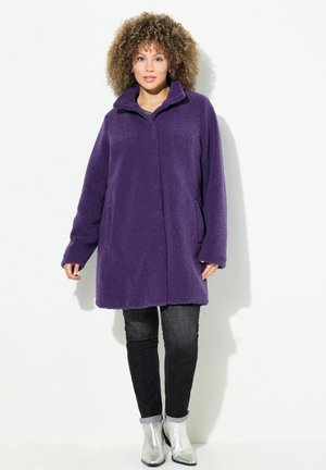 Purple fleece coat with a high collar, long sleeves, and side pockets, paired with dark jeans and silver ankle boots. Smooth texture.
