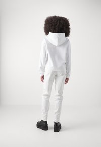 Bílá mikina s kapucí na šňůrky, ve spojení s bílými kalhotami a černými platformovými botami. Hladká textura, neformální design, minimalistický styl.