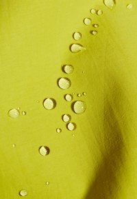 Waterdruppels parelen op een heldergele, gestructureerde, waterbestendige stof.