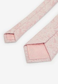 Cravate rose avec des motifs paisley blancs complexes, présentant une texture lisse et des pointes angulaires, mettant en avant un design de tissu détaillé.
