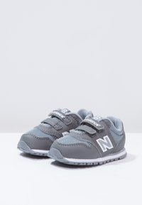 Szare dziecięce trampki z siatki i syntetycznych osłon, z rzepami i białą podeszwą. Charakteryzują się wyraźnym logo "N" po bokach.