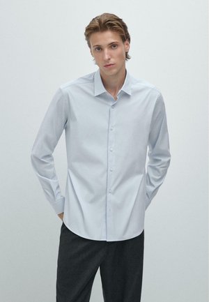 Chemise bleu clair à manches longues, col étalé et texture lisse. Assortie à un pantalon gris foncé.