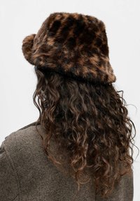 Faux fur-buckethatt i brunt med ett leopardmönster. Mjuk textur och något utåtböjd skärm. Bärs tillsammans med en texturerad brun jacka.
