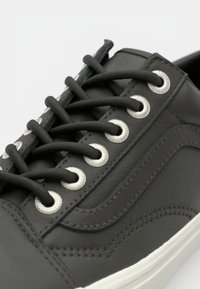 Zapatilla de deporte gris oscuro con parte superior de cuero suave, suela de goma blanca, cordones negros, ojales de metal y un sutil patrón de olas en el lateral.
