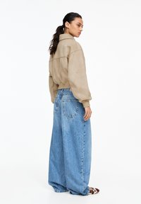 Beige mockastövel oversized jacka som matchar med löst sittande, ljusblå denimjeans med bakfickor och en blekt textur.