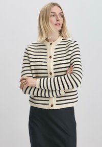 Gebreide cardigan met horizontale marineblauwe en crèmekleurige strepen, ronde hals, knoopsluiting aan de voorkant en geribbelde manchetten. Voorzien van houten knopen.