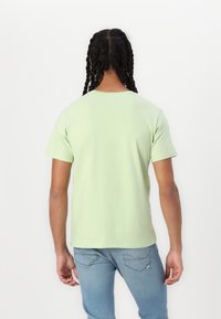 Lys grøn bomulds t-shirt med korte ærmer, rund halsudskæring og en afslappet pasform, set bagfra. Båret med blå jeans.