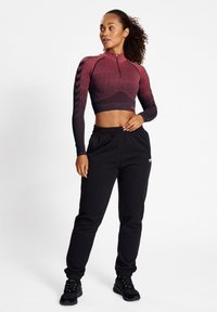 Sportliches, kurzes Oberteil in einem Farbverlauf von Rot zu Schwarz mit Reißverschluss, kombiniert mit schwarzen Jogginghosen mit elastischen Bündchen und Logo-Akzenten.