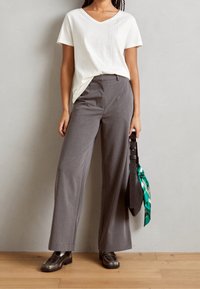 Camiseta blanca de cuello en v con detalle de rayas verticales, combinada con pantalones de pierna ancha gris. Los accesorios incluyen un cinturón negro y una bufanda verde con patrón.