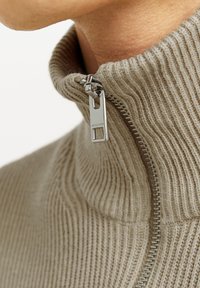 Bežinis dryžuotas zip-up megztinis su aukštu apykakle, turintis sidabrinį metalinį užtrauktuką ir tekstūruotą medžiagą, pabrėžiantis patogų prigludimą aplink kaklą.
