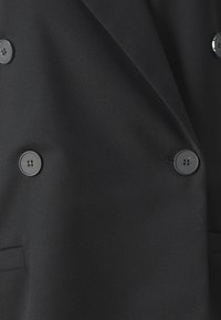 Sacou negru, croit pe măsură, dintr-un material texturat, cu design cu guler dublu și patru butoane mari, rotunde, plus două buzunare laterale.