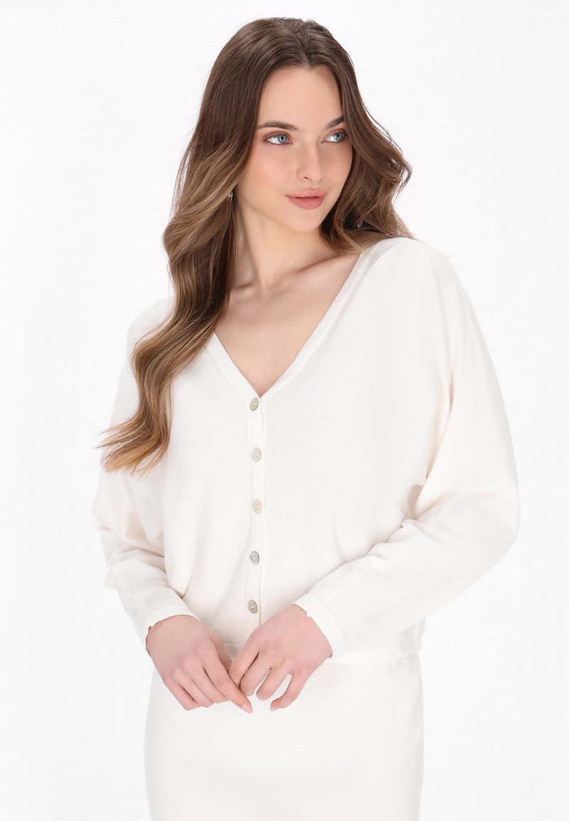 Lange mouw v-hals cardigan in zacht witte stof, met een knoopsluiting aan de voorkant en een relaxte pasvorm, voorzien van fijne stiksels langs de manchetten.