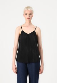 Svart plissert cami med tynne stropper og V-hals, laget av lett stoff. Brukt sammen med løse denimbukser.
