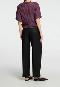 Person wearing a purple short-sleeve knit top, black wide-leg pants, and black slingback flat shoes, standing against a plain white background.