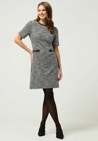 Abito a maniche corte con motivo houndstooth bianco e nero; presenta una vita aderente, tasche laterali con bottoni e un orlo a ginocchio.