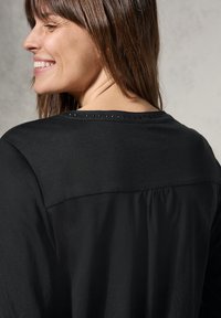 Top nero con una vestibilità comoda, realizzato in tessuto morbido, con una schiena plissettata e borchie decorative lungo il collo.