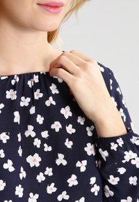 Navy blouse with a gathered neckline, featuring a white and pink floral pattern. Long sleeves with elastic cuffs. Light fabric texture.
