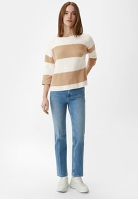 Sukienka w paski w odcieniach kremowym i beżowym z teksturowanym splotem, z rękawami 3/4, w połączeniu z jasnoniebieskimi dżinsami i białymi trampkami.