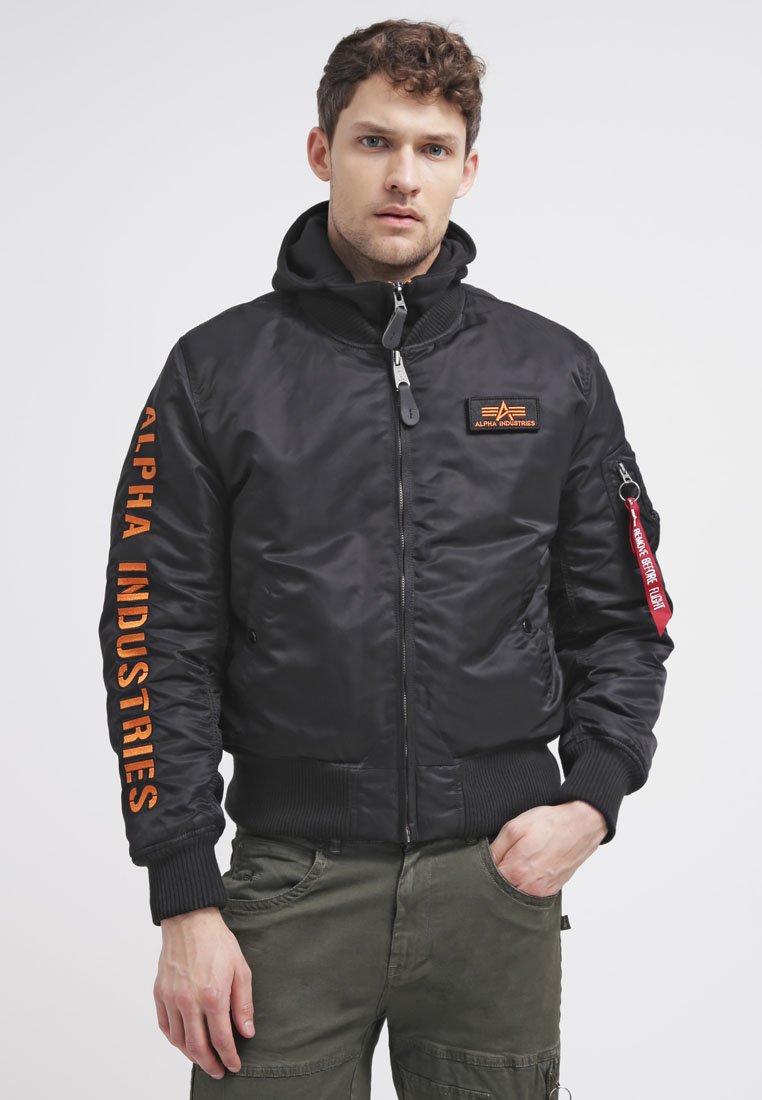 Must svart bomber-jakk, millel on oranž "Alpha Industries" tekst varrukal, tõmblukuga taskud, soonikkoes mansetid ja krae. Sisaldab eemaldatavat kapuutsi.