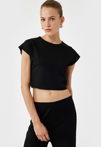 Top court noir à manches courtes, en tissu texturé, avec un col rond, associé à un pantalon assorti, créant une tenue simple et coordonnée.