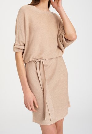 Beige gebreide jurk met een losse pasvorm, korte mouwen en een taillekoord. Heeft een subtiele glans en een zijsplit voor extra detail.