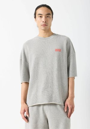 Hall hallikas ülepaisutatud dressipluus pehmest materjalist, millel on ümmargune kaelus, lühikesed varrukad ja väikene punane "American Vintage" logo rinnal.