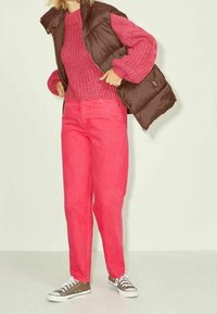 Pull en tricot rose, gilet rembourré marron et pantalon rose vif associés à des baskets marron. Texture lisse, coupe décontractée, design en couches.