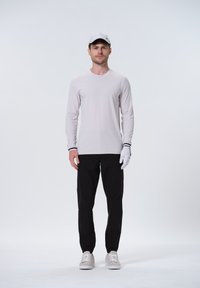 Lys grå langærmet skjorte med et subtilt mønster, sorte bukser og hvide handsker; lys grå kasket, grå sneakers med hvide såler.