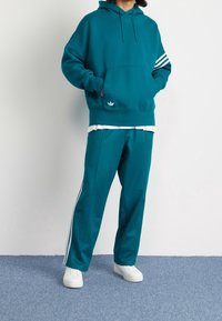 Teal huvtröja med framficka, dragsko i huvan och vit logotyp. Matchas med matchande tealbyxor med vita sidostråk och elastisk midja.