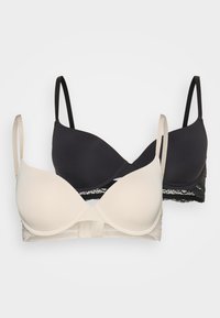 Deux soutiens-gorge : un crème, un noir. Les deux possèdent des bonnets lisses et rembourrés, des bretelles réglables, et des détails en dentelle le long de la bande.