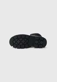 Fekete gumi csizma talp, mely a tapadás és tartósság javítása érdekében texturált mintázattal rendelkezik, mély barázdákkal és téglalap alakú kiemelkedésekkel.